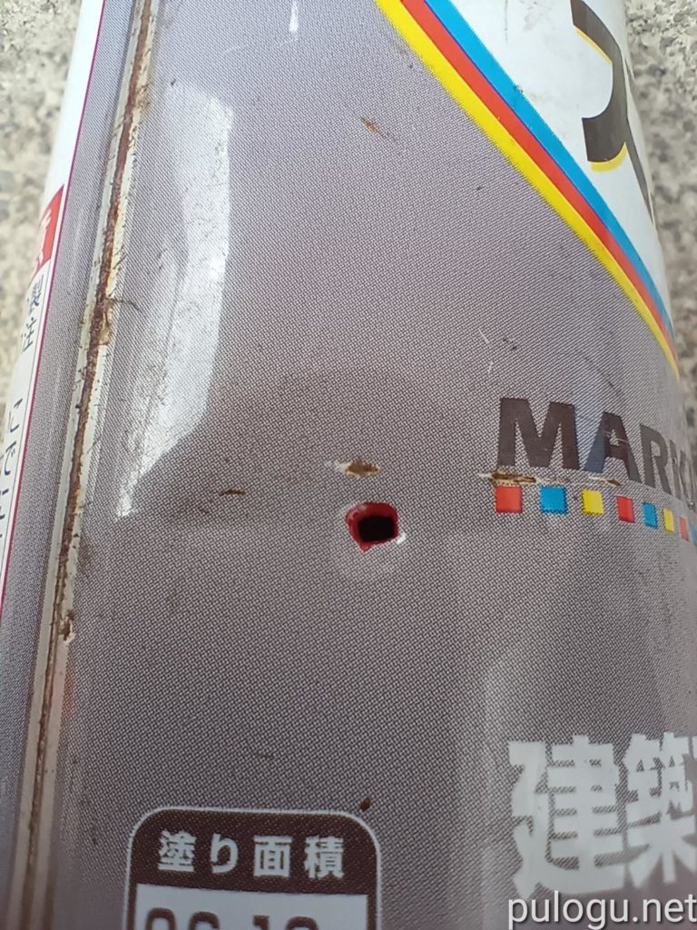 色のスプレー缶に穴が開いています。中の赤の塗料がにじみ出ています。